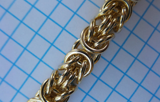 Gold Byzantine chainmaille close-up on blue graph paper