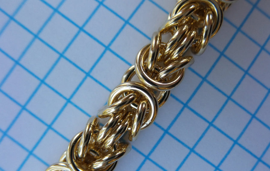 Gold Byzantine chainmaille close-up on blue graph paper