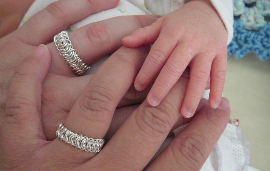 Two sterling silver Perfect Ring chainmaille rings on hands holding a baby’s hand, Urban Maille
